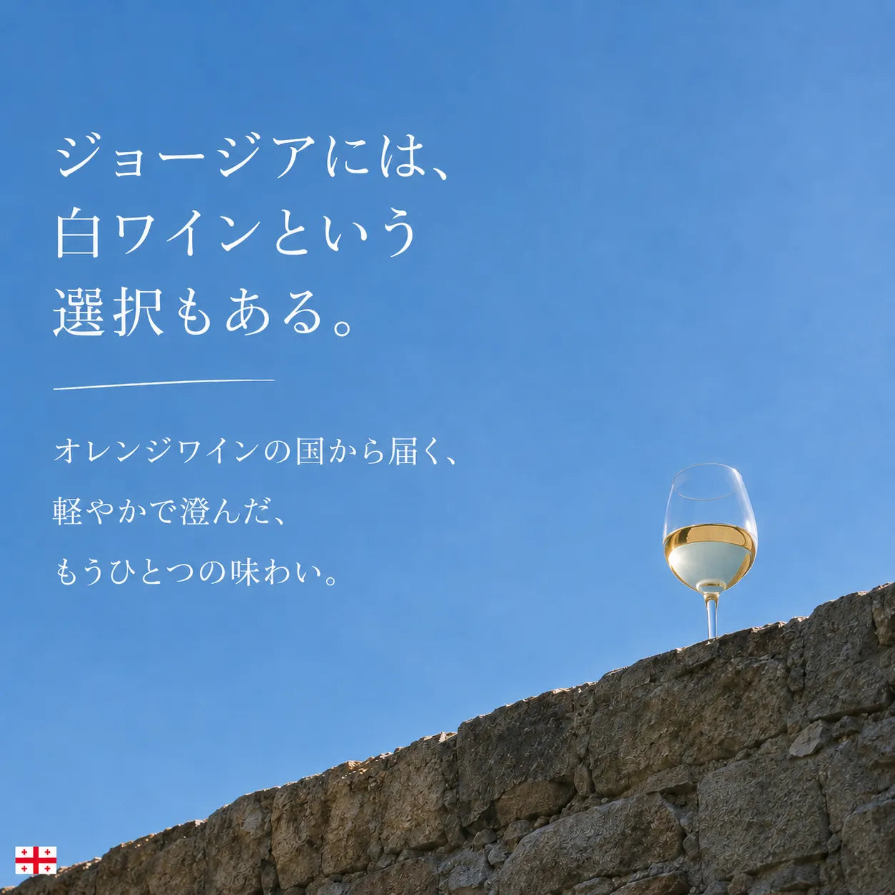 ジョージアには白ワインという選択もあると伝える青空と石壁の上のグラス