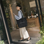 ブラックのトートバッグでナチュラルワインの店を訪れる女性、ガラス張りの店先